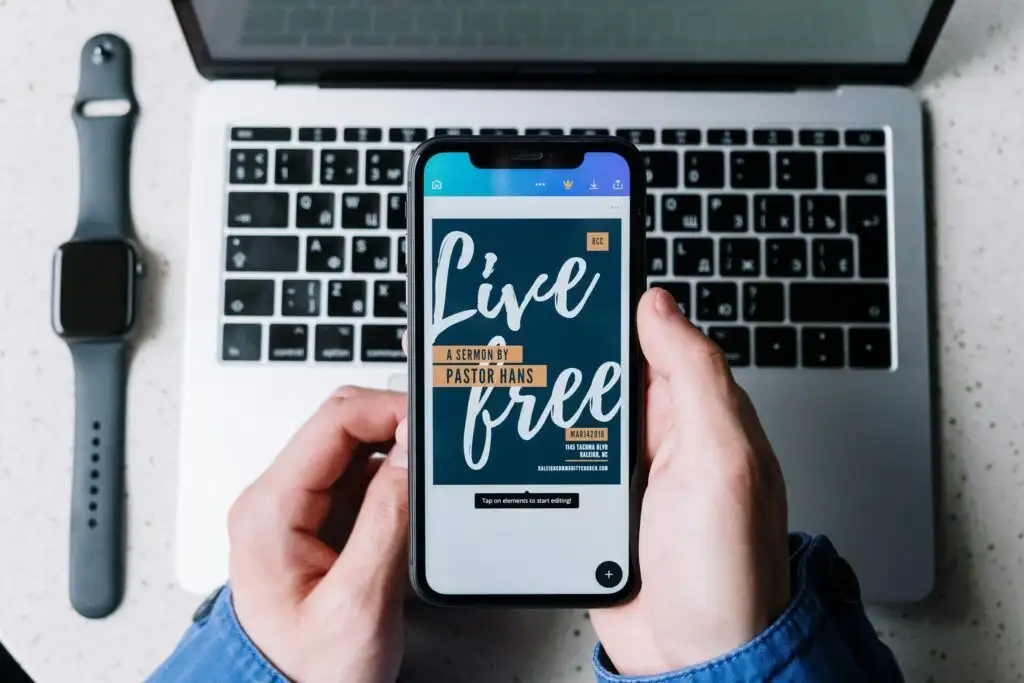 Overhead view of a smartphone displaying 'Live Free' on a laptop keyboard, beside a smartwatch.