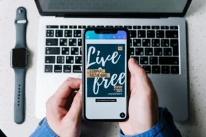 Overhead view of a smartphone displaying 'Live Free' on a laptop keyboard, beside a smartwatch.